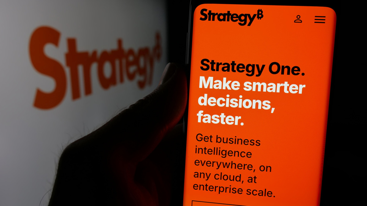 Person holding smartphone with web page of US company MicroStrategy Inc. on screen in front of logo. Focus on center of phone display.