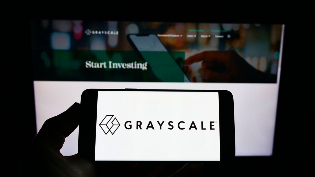 Person holding mobile phone with logo of crypto currency company Grayscale Investments LLC on screen in front of web page. Focus on phone display.