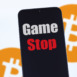 Close up on the logo gameStop, in the blurred background, two instances of the bitcoin logo