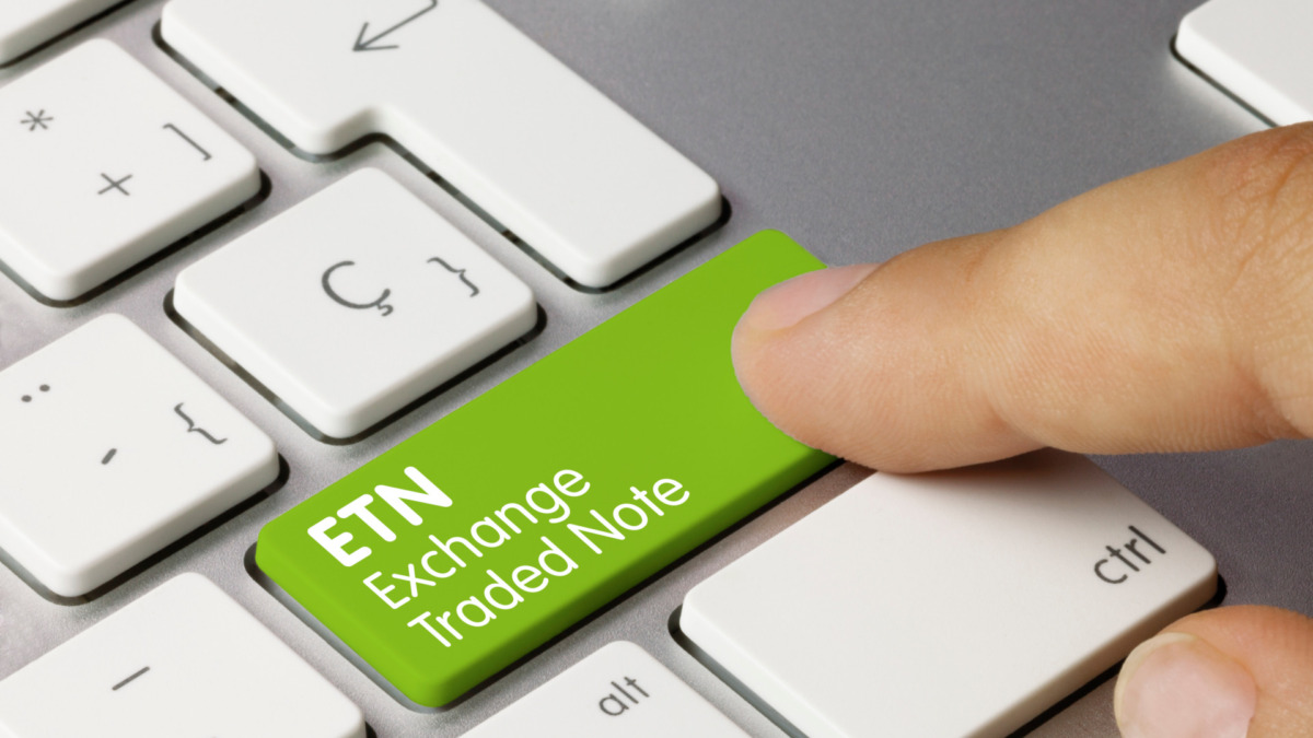 ETN Exchange traded note Written on Green Key of Metallic Keyboard. Finger pressing key.