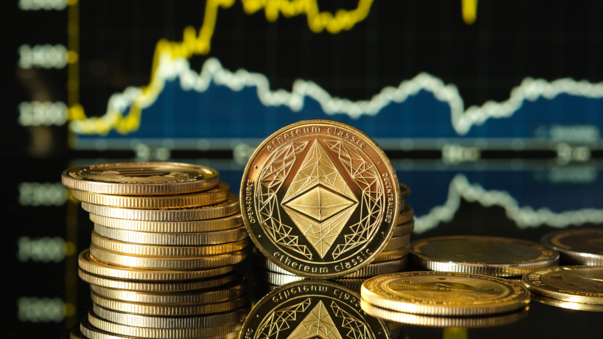 Piles of shiny ethereum coins are elegantly arranged on a reflective surface, while charts show cryptocurrency trends in the background