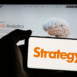 Person holding mobile phone with logo of US company MicroStrategy Inc. on screen in front of web page. Focus on phone display.