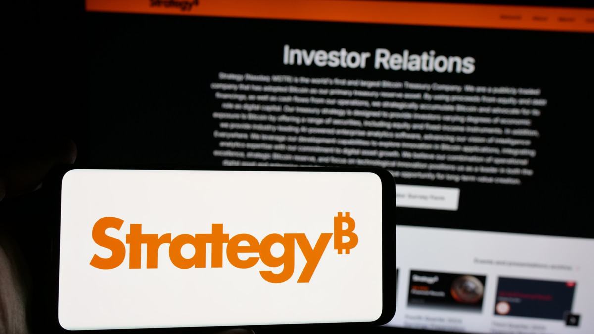 Person holding smartphone with logo of US company MicroStrategy Inc. on screen in front of website. Focus on phone display.