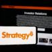 Person holding smartphone with logo of US company MicroStrategy Inc. on screen in front of website. Focus on phone display.