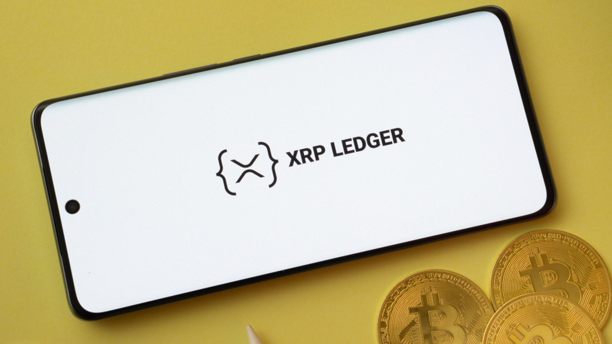 XRP Ledger logo on smartphone screen near Bitcoin coin and QR code on background.