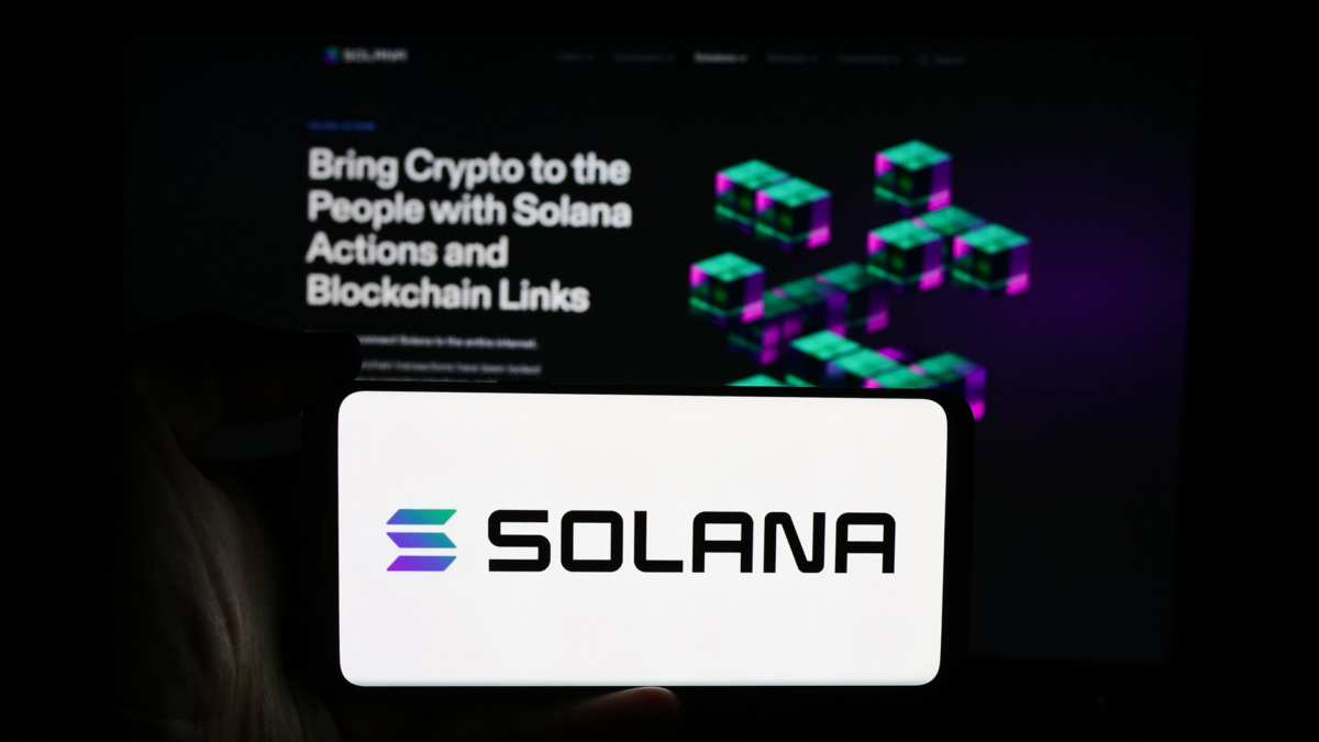 erson holding cellphone with logo of blockchain platform company Solana in front of business webpage. Focus on phone display.