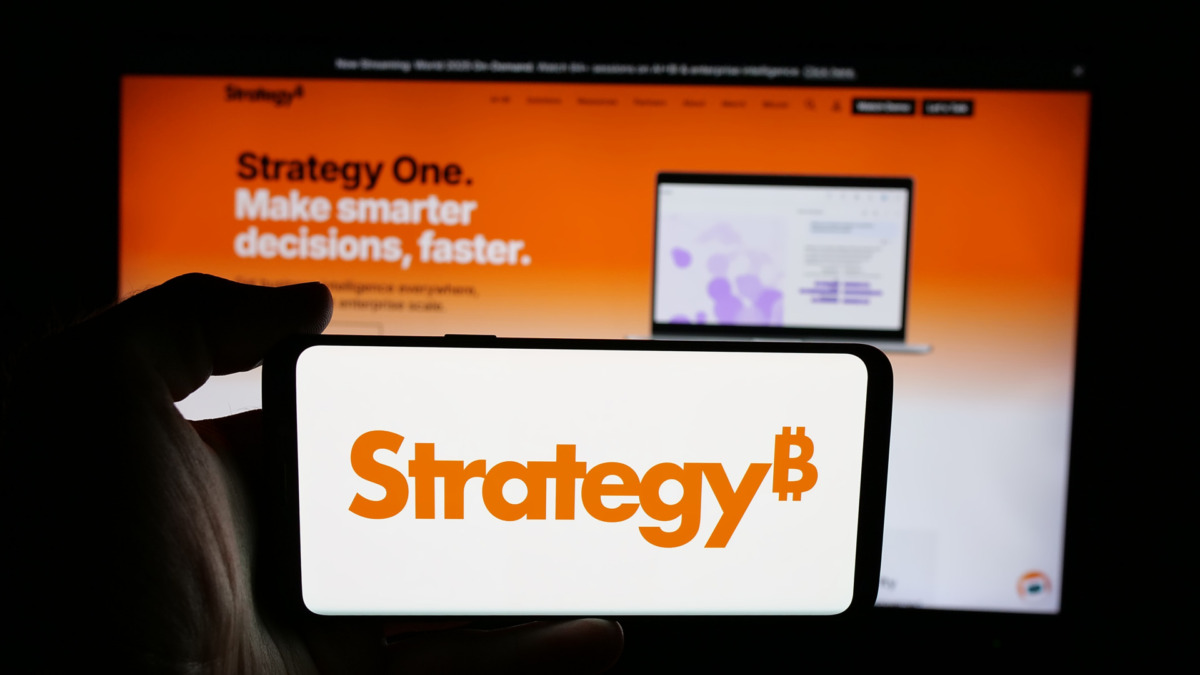 Person holding cellphone with logo of US company MicroStrategy Inc. on screen in front of webpage. Focus on phone display.