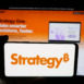 Person holding cellphone with logo of US company MicroStrategy Inc. on screen in front of webpage. Focus on phone display.
