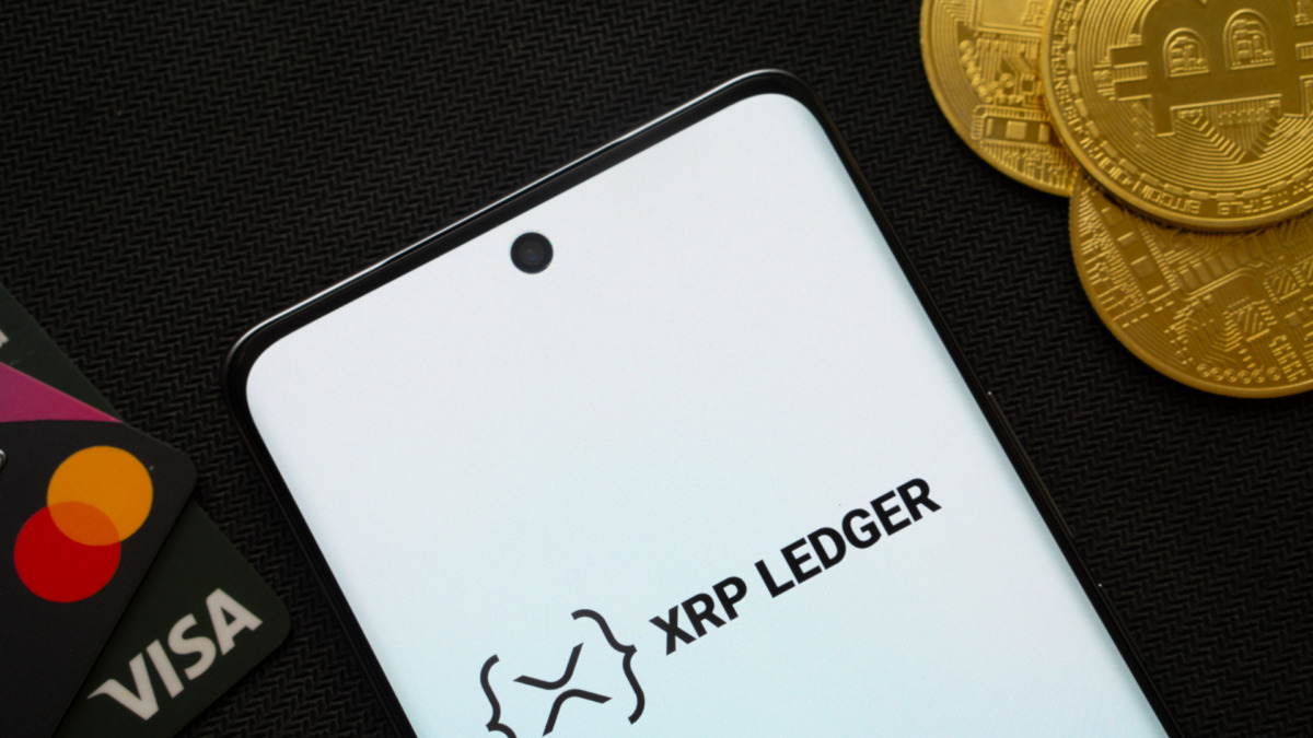 Smartphone displaying XRP Ledger logo surrounded by Bitcoin coins and payment cards.