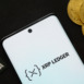 Smartphone displaying XRP Ledger logo surrounded by Bitcoin coins and payment cards.