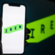Silhouette of Hand Holding iPhone with IREN Logo in Front of Computer Screen Displaying Logo – Energy and Utilities Provider (IREN)