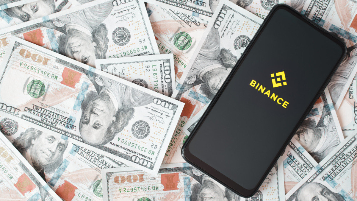 Binance mobile application of global blockchain ecosystem, cryptocurrency exchange. Binance logo on screen of smartphone lying on money background. Top view, copy space. Smolensk, Russia 28.02.2022.