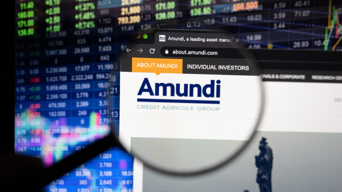 Amundi company logo on a website with blurry stock market developments in the background, seen on a computer screen through a magnifying glass