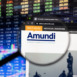 Amundi company logo on a website with blurry stock market developments in the background, seen on a computer screen through a magnifying glass