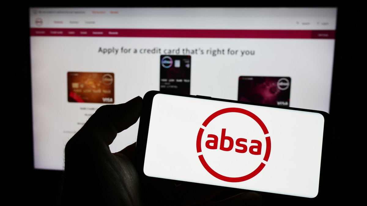 Person holding mobile phone with logo of South African company Absa Group Limited on screen in front of business web page. Focus on phone display.