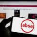 Person holding mobile phone with logo of South African company Absa Group Limited on screen in front of business web page. Focus on phone display.