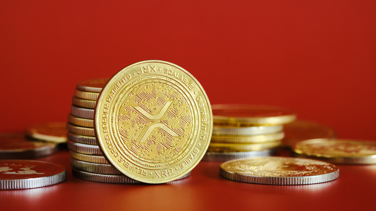 A collection of gold XRP cryptocurrencies is prominently displayed against a bright red background. The coins represent digital currency concepts and emphasize finance and investment.