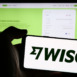 Person holding mobile phone with logo of British financial technology company Wise plc in front of business web page. Focus on phone display.
