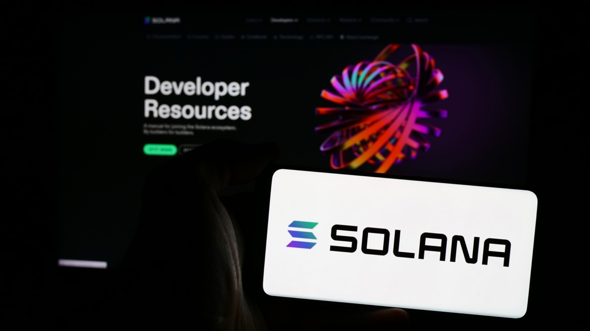Person holding mobile phone with logo of blockchain platform company Solana in front of business web page. Focus on phone display.