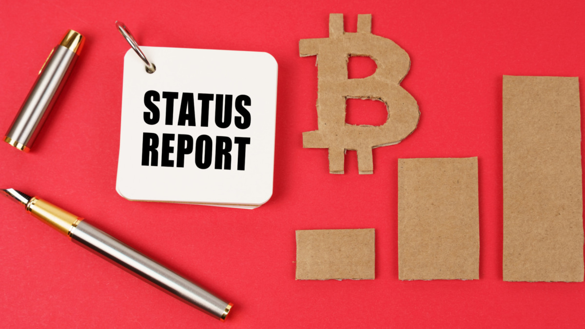 Business and bitcoin concept. On a red surface lie a bitcoin symbol, a graph, a pen and a notepad with the inscription - STATUS REPORT