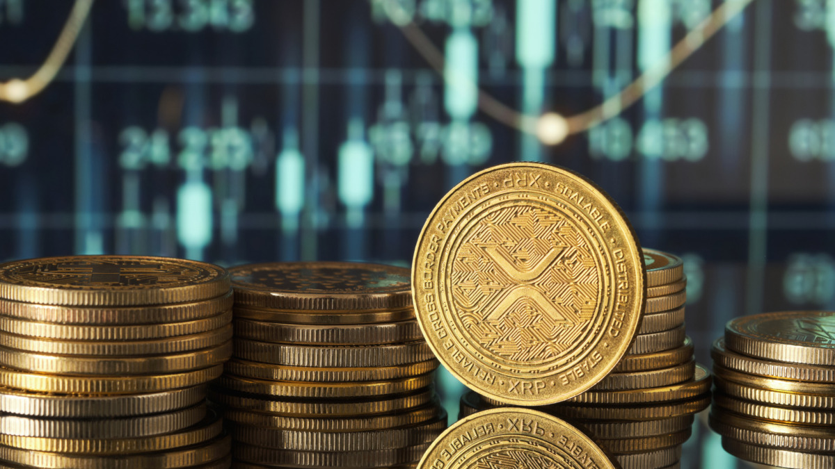 Golden XRP coins are displayed in front of green and blue financial graphs representing market trends and cryptocurrency fluctuations in a modern setting.