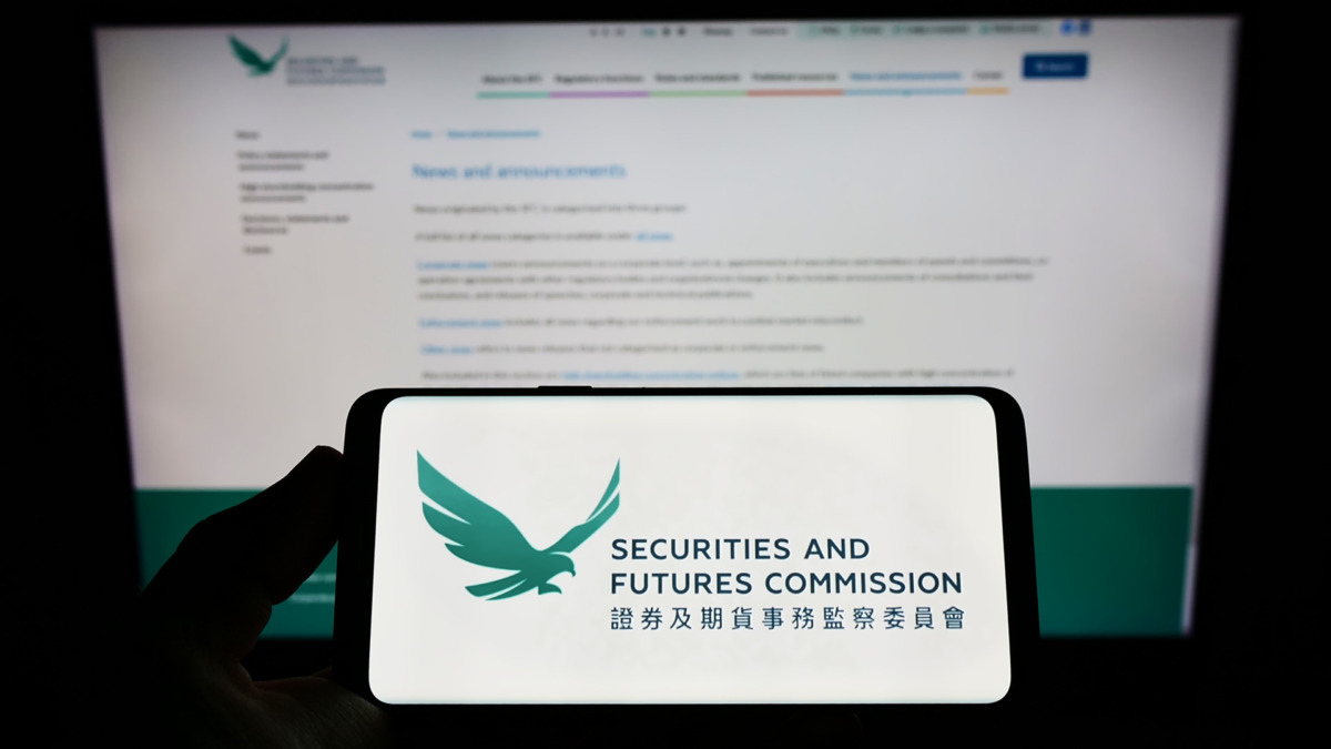 Person holding smartphone with logo of Hong Kong Securities and Futures Commission (SFC) on screen in front of website. Focus on phone display.