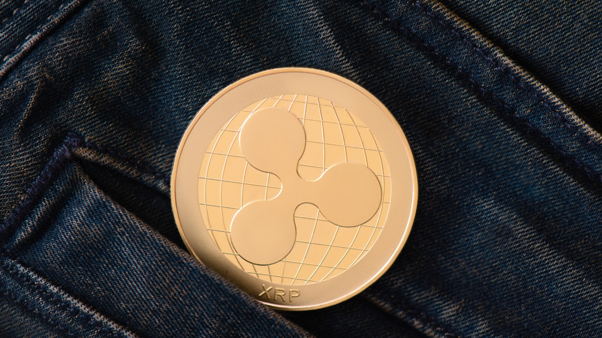 A golden Ripple cryptocurrency coin protrudes from the pocket of blue frayed jeans. Virtual money into reality concept. Exchange, withdrawal and save of cryptocurrencies from virtual to reality.