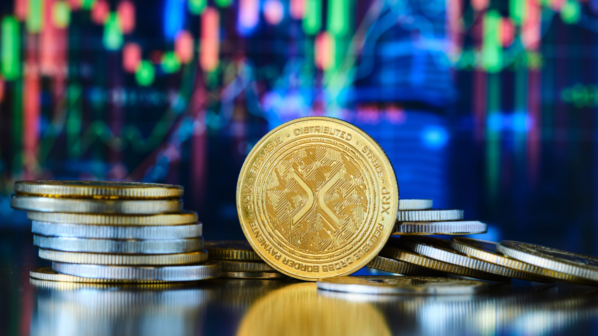 Piles of gold-colored Xrp coins take center stage. A digital graph in the background shows trends and fluctuating market data.