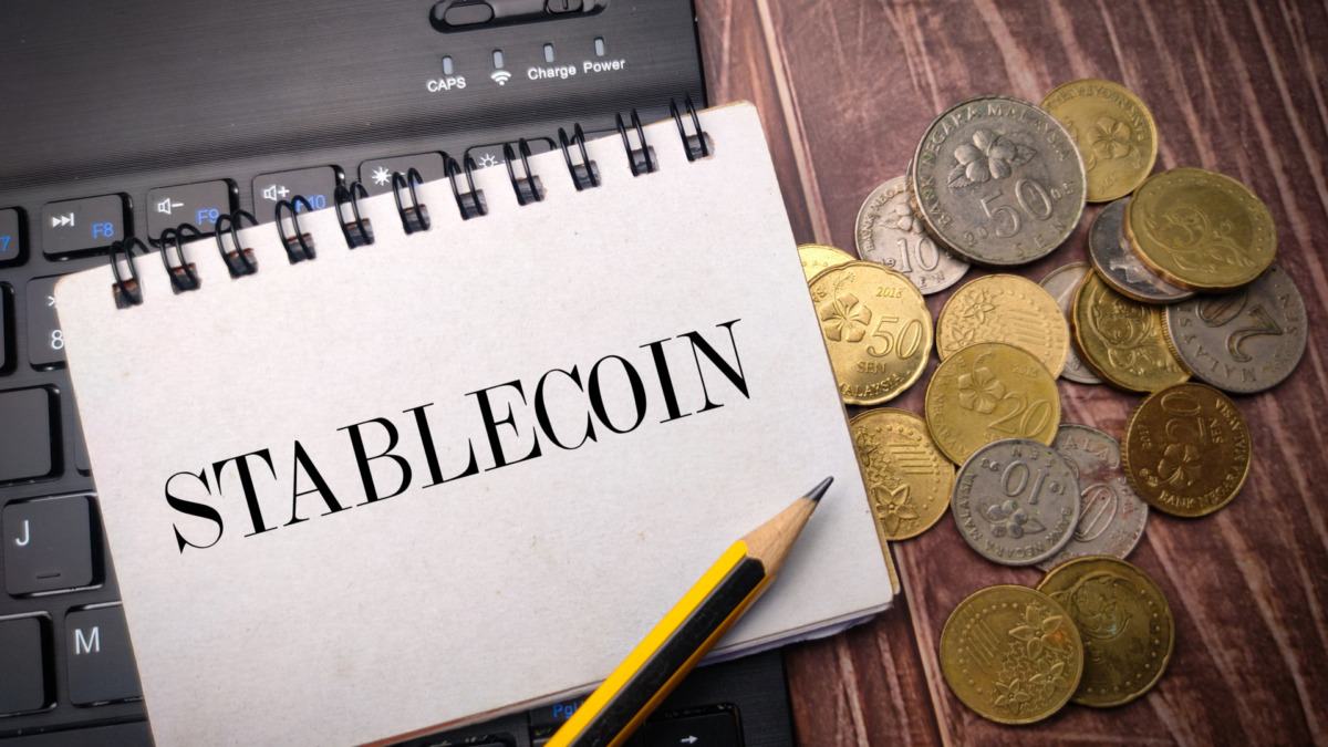 Notebook and coins on a wooden background with the word STABLECOIN.