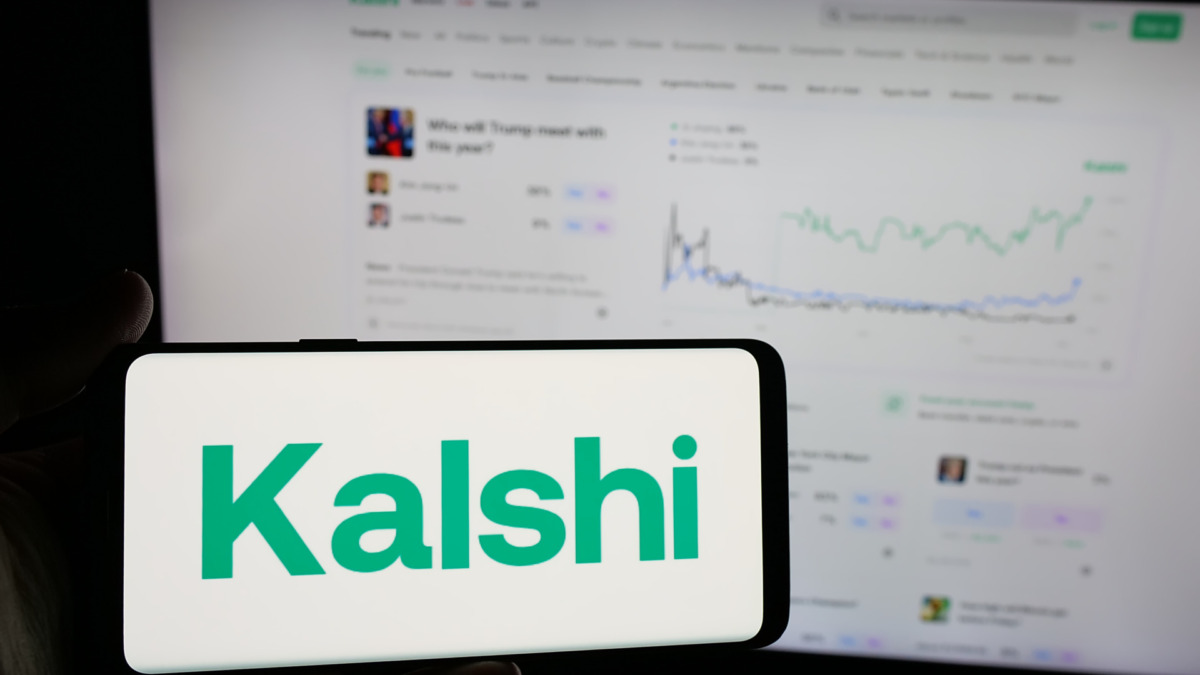 Person holding smartphone with logo of US prediction market company Kalshi Inc. on screen in front of website. Focus on phone display.