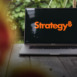 The new MicroStrategy (Strategy Inc.) logo shown on a MacBook Pro screen, representing innovation and modern business technology.
