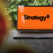The new MicroStrategy (Strategy Inc.) logo shown on a MacBook Pro screen, representing innovation and modern business technology.