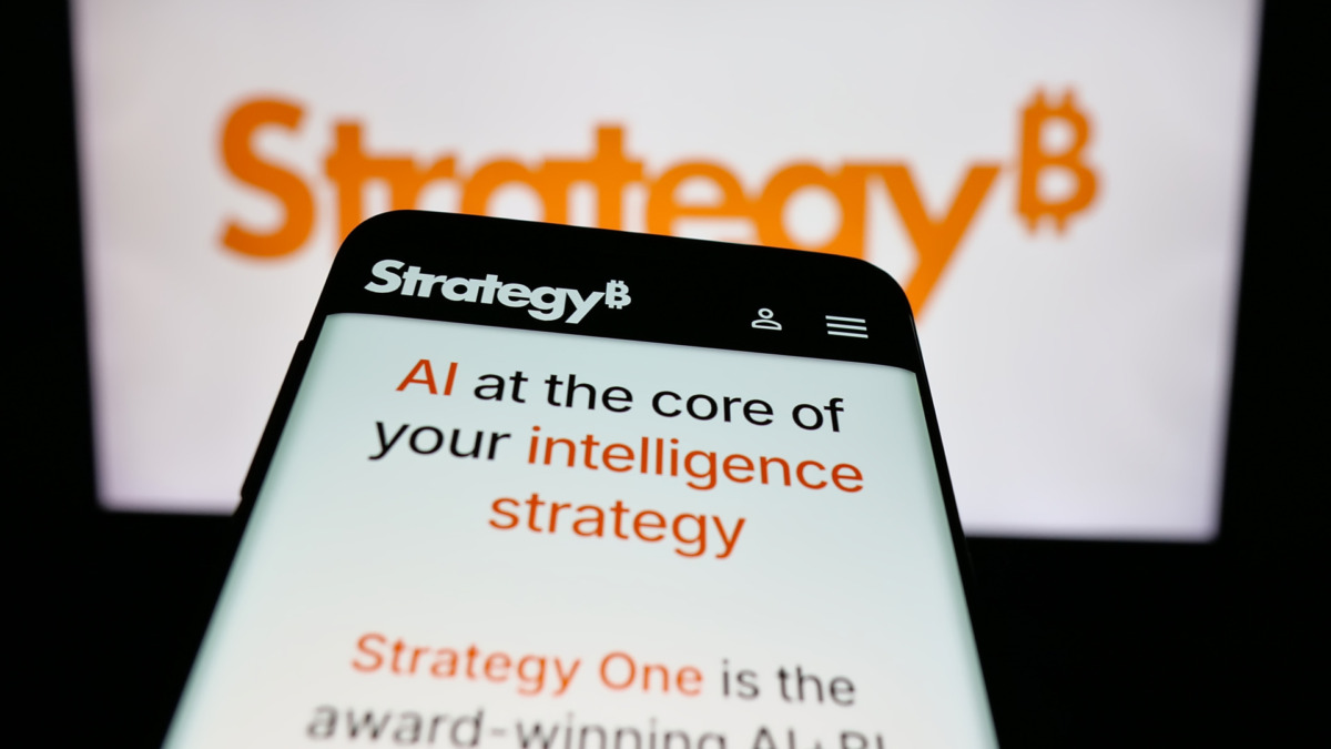 Mobile phone with website of US company MicroStrategy Inc. on screen in front of logo. Focus on top-left of phone display.
