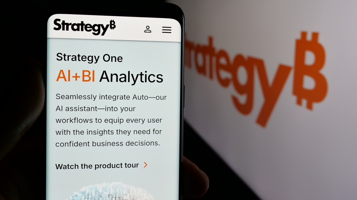 Person holding cellphone with webpage of US company MicroStrategy Inc. on screen in front of logo. Focus on center of phone display.