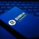 Closeup of a dark blue smartphone displaying the bitmine logo and text, resting on a laptop keyboard in a dimly lit, bluetoned environment , New York City, 15 December 2025