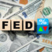 Wooden blocks spelling FED placed on U.S. dollar bills, alongside green up and red down arrows, symbolizing Federal Reserve interest rate decisions and their effect on the economy.