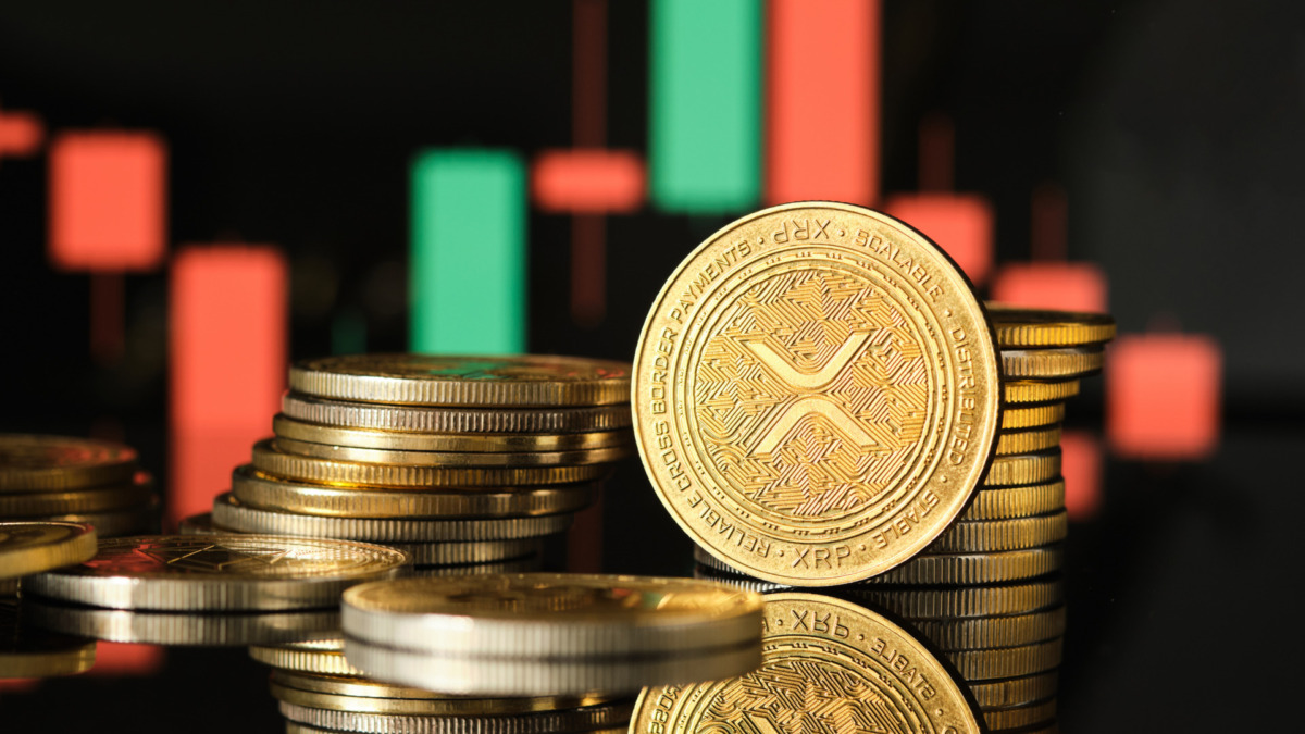 Several XRP cryptocurrency coins are arranged in stacks, reflecting light, against a backdrop of a vibrant trading chart showing market trends and fluctuations.
