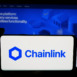 Stuttgart, Germany - 12-16-2025: Person holding cellphone with logo of blockchain oracle network Chainlink on screen in front of webpage. Focus on phone display.