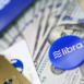 Minsk, Belarus, - June 09, 2019: Blue chip with libra sign lying on big pile of US dollars with facebook apps on cellphone in background close-up