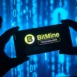 Silhouetted hands holding smartphone with BitMine logo on screen