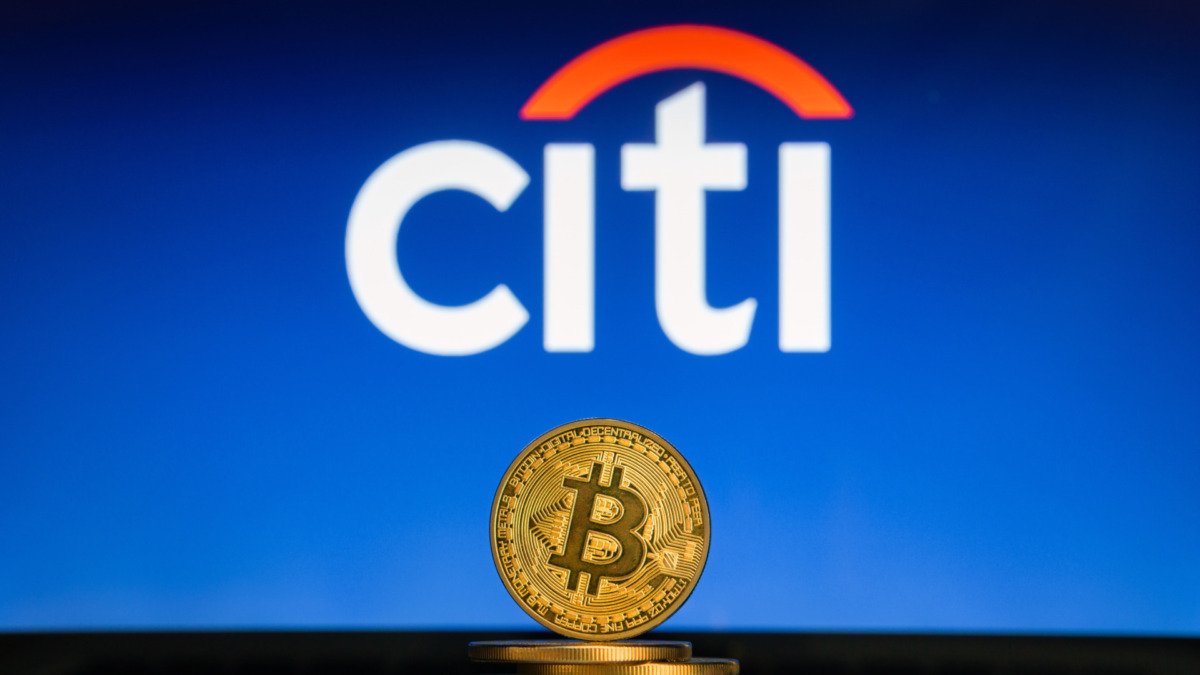 Bitcoin on a stack of coins with Citi Bank logo on a laptop screen.