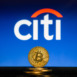 Bitcoin on a stack of coins with Citi Bank logo on a laptop screen.