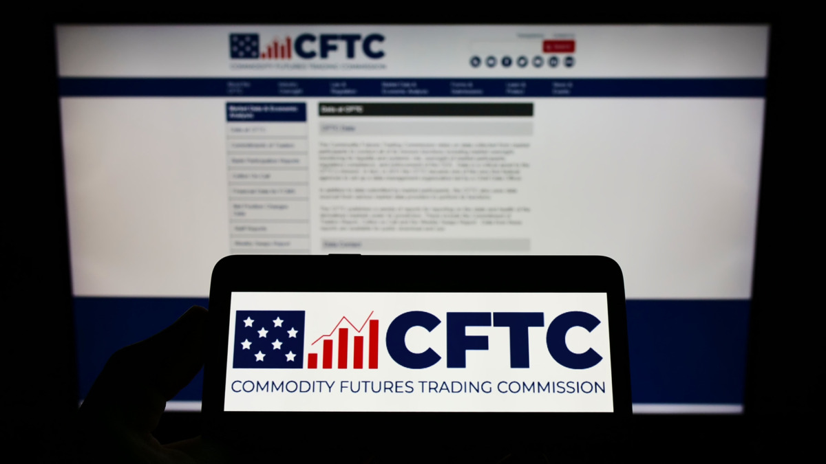 Person holding cellphone with logo of American Commodity Futures Trading Commission (CFTC) on screen in front of webpage. Focus on phone display.